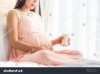 pregnant-woman-holding-glass-of-fresh-milk-&-touching-her-belly-with-care-by-window-739402951.jpg