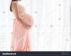 beautiful-pregnant-woman-holding-belly-near-window-at-home-734777401.jpg