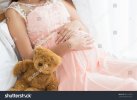 pregnant-woman-in-pink-dress-and-teddy-bear-on-the-bed-in-bedroom-781151959.jpg