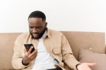 annoyed-african-american-man-yelling-phone-while-sitting-sofa-home-angry-man-looks-phone-while...jpg